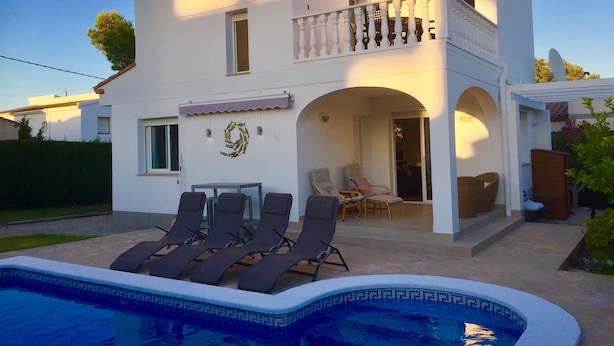 Ein zweistöckiges Gebäude mit einem Balkon, einem Schwimmbecken und Sitzgelegenheiten im Freien.