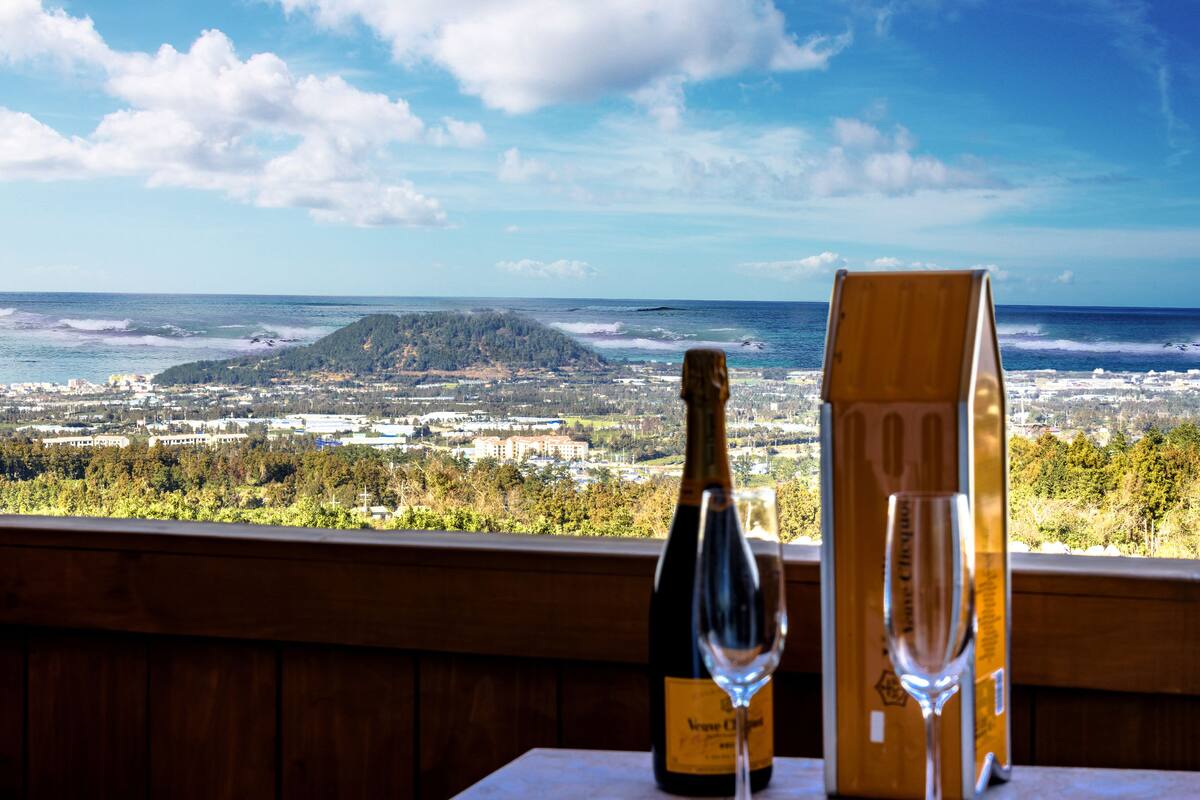 Ein Tisch mit einer Weinflasche und einem Glas, mit Blick auf die Küste, ein Berg und eine Stadtlandschaft.