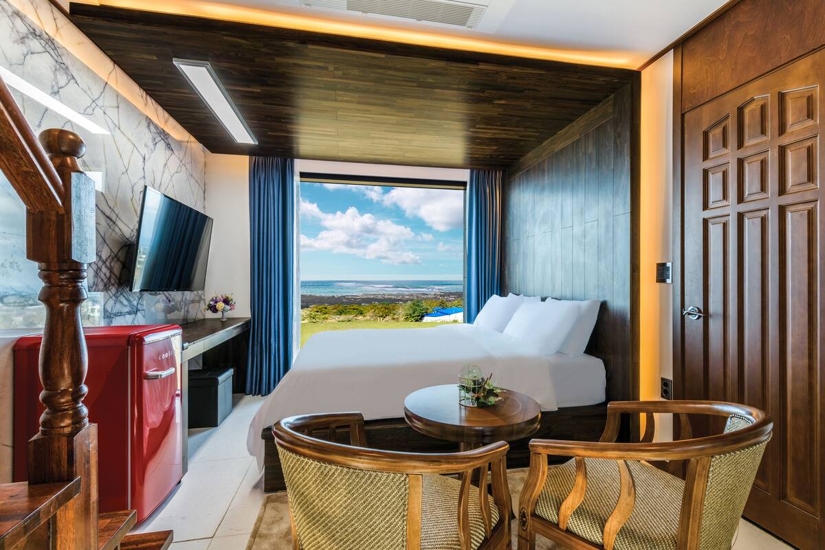 Ein Hotelzimmer mit einem großen Bett, einem Schreibtisch mit Fernseher und Blick auf die Landschaft, sowie einer Holztür.