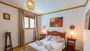 Een slaapkamer met een houten bed, twee nachtkastjes met lampen, een raam met gordijnen, en een schilderij aan de muur.