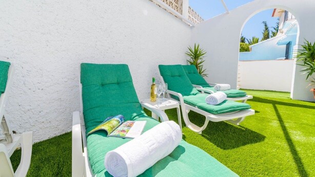 Een zonnig terras met groene fauteuils, een bijzettafeltje met een fles en glazen, en een tijdschrift.