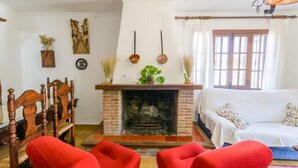 Een woonkamer met een open haard, een bank, een eettafel met stoelen en decoratieve items aan de muren.