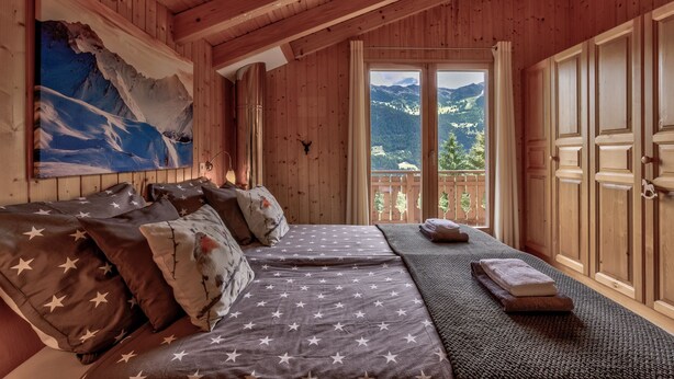 Une chambre rustique en bois, avec un lit, un tableau représentant des montagnes et un balcon offrant une vue sur les montagnes.