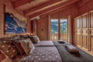Ein Zimmer in einer Holzhütte mit einem Bett, einem Berg-Gemälde und einem Balkon mit Bergblick.