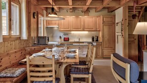 Un intérieur en bois comprenant une table à manger pour quatre personnes, des armoires en bois et un coin cuisine avec une cuisinière et un évier.