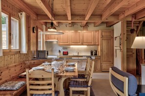 Un intérieur en bois comprenant une table à manger pour quatre personnes, des armoires en bois et un coin cuisine avec une cuisinière et un évier.