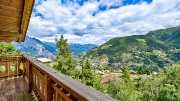 Un balcon en bois offrant une vue sur un paysage montagneux et un petit village situé en contrebas.