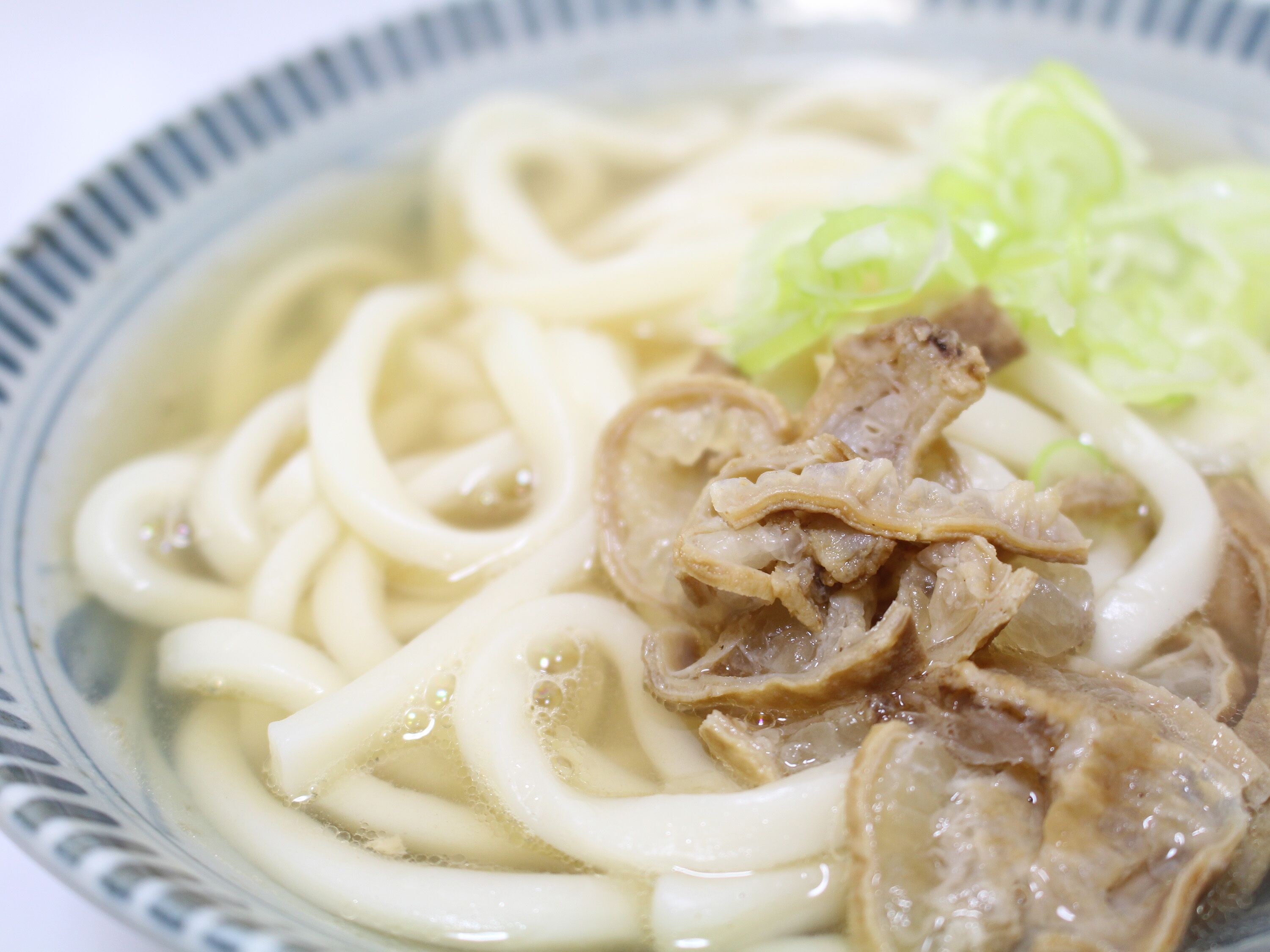 Un tazón de ramen con fideos, carne y cebolletas.
