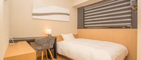 A compact hotel room with a bed, a desk, and a chair.