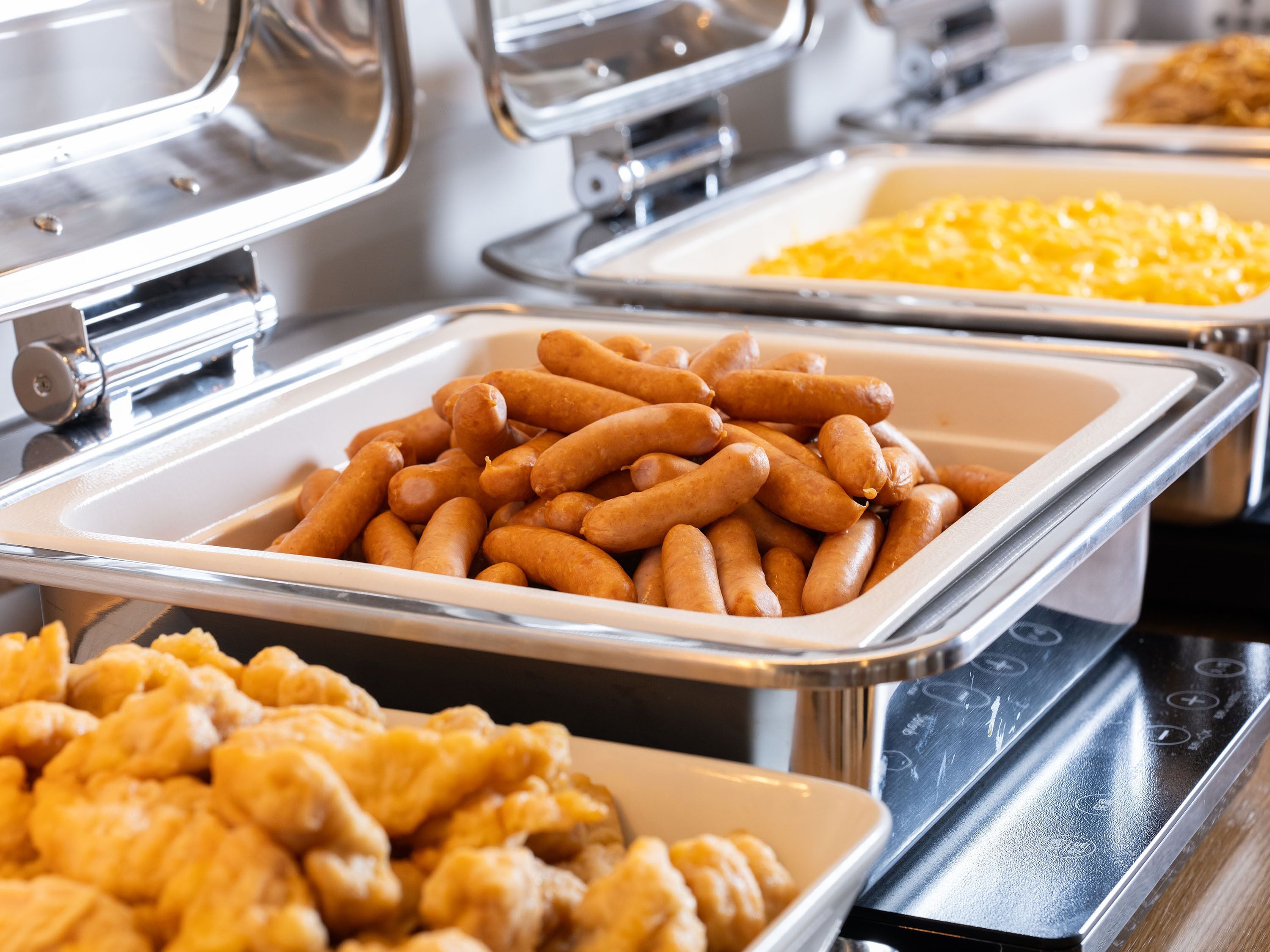 Un buffet proposant une variété de plats, notamment des saucisses, des macaronis et du poulet frit.