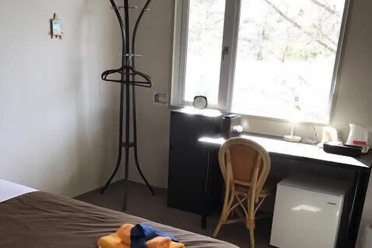 A hotel room with a bed, a desk, a chair, and a small refrigerator.