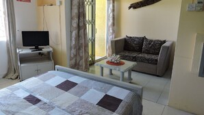 A hotel room with a bed, a desk with a computer, a sofa, and a small table with a decorative item. - Apartment in residence (Blue Bay)