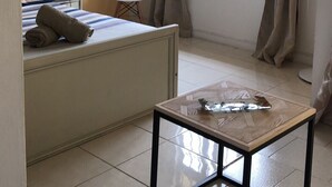 A hotel room with a bed, a small table, a ceiling fan, a window with curtains, and a wall-mounted TV. - Apartment in residence (Blue Bay)