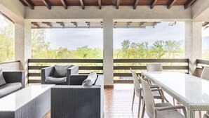 Un patio al aire libre con mobiliario de mimbre, una mesa y vistas a follaje.