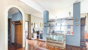 Amplia sala de estar con piso de madera, un tapete estampado, un sofá y una estantería.