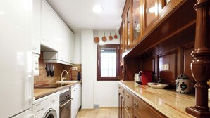 A kitchen with a washing machine, wooden cabinets, and a window. - Arrayán. 3 bedrooms  in Macarena (Sevilla)