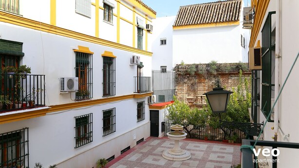 A courtyard with a fountain, white buildings with yellow trim, and a tiled roof. - Arrayán. 3 bedrooms  in Macarena (Sevilla)