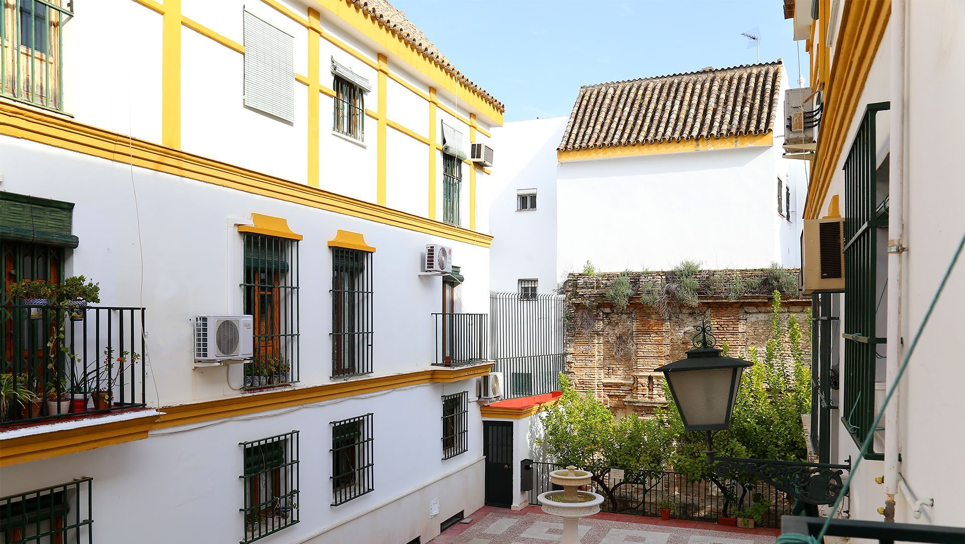 A courtyard with a fountain, white buildings with yellow trim, and a tiled roof.