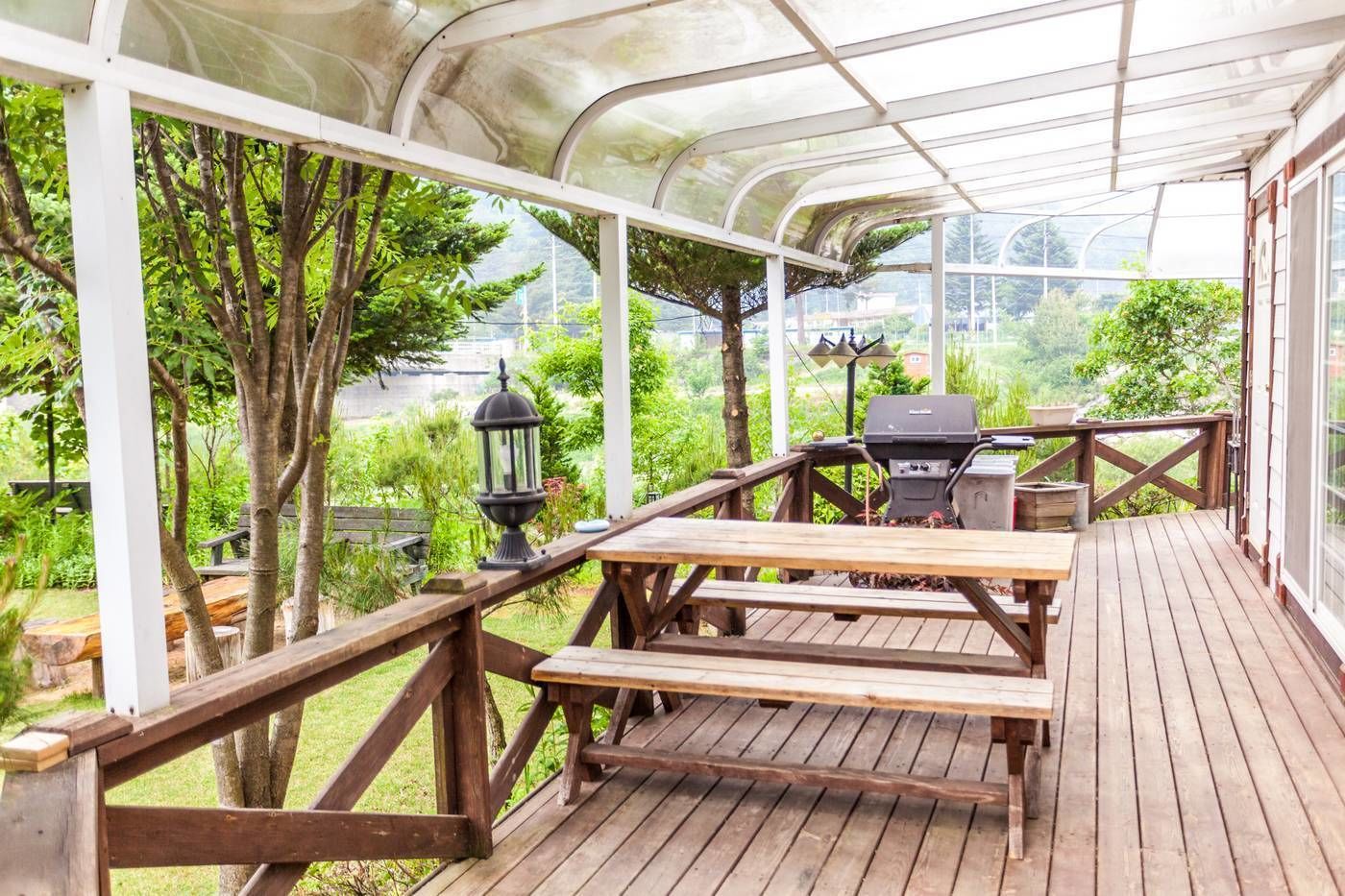 A covered outdoor patio with wooden tables and benches, a grill, and a lantern.