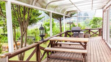 A covered outdoor patio with wooden tables and benches, a grill, and a lantern.