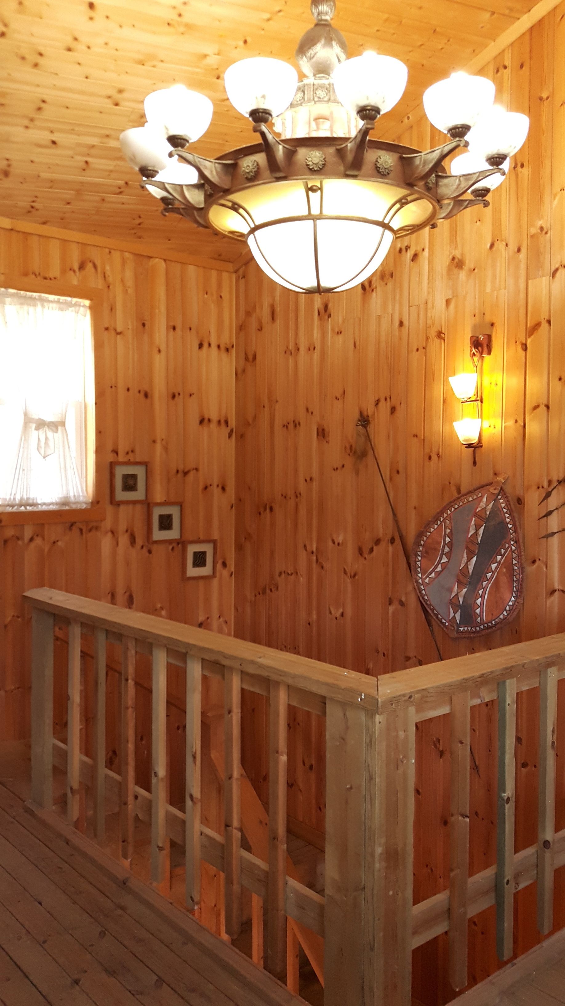 A wooden interior with a staircase, a chandelier, and wall-mounted lights.