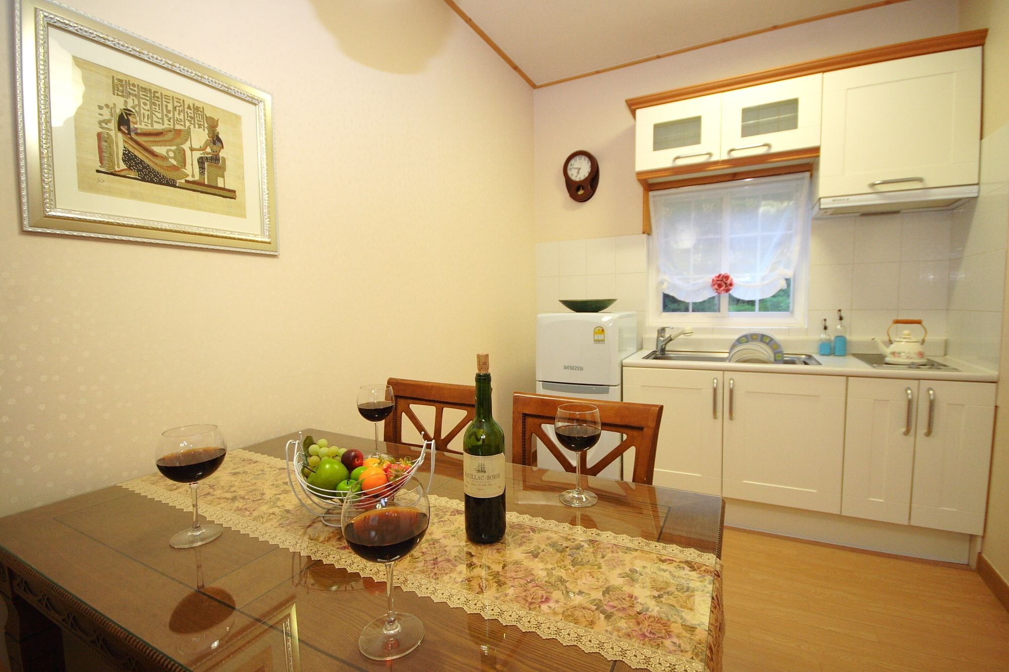 A dining area with a table set for two, featuring wine glasses, a bottle of wine, and a fruit bowl.