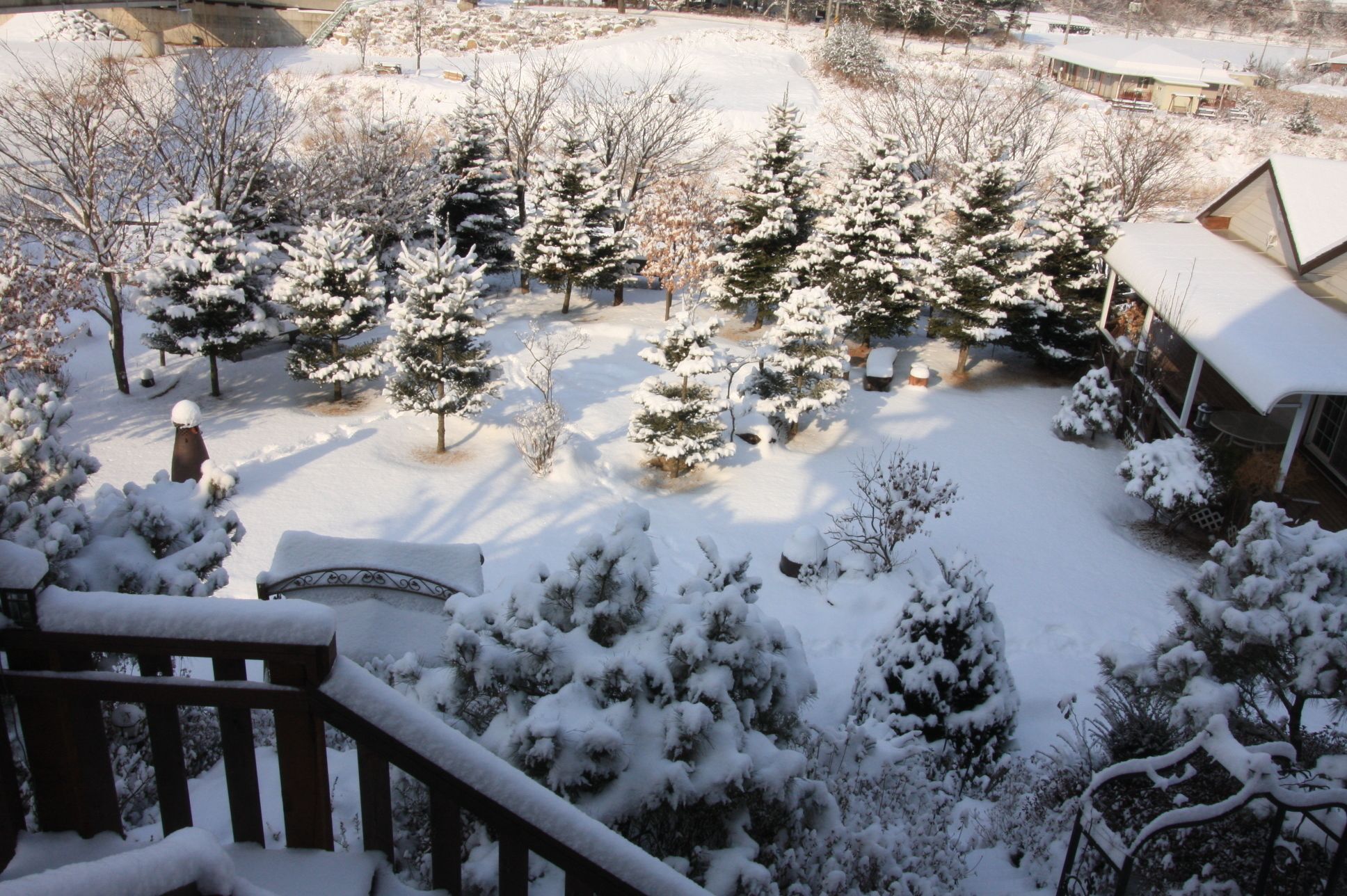 Un paysage enneigé avec une terrasse en bois et une vue sur une maison dont le toit est recouvert de neige.