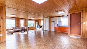 Quarto espaçoso com piso de madeira, sofá, televisão e cozinha com armários laranja.