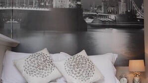 Hotelkamer met een bed, kussens, dekbed, nachtkastje met een lamp en een muurschildering van een brug.