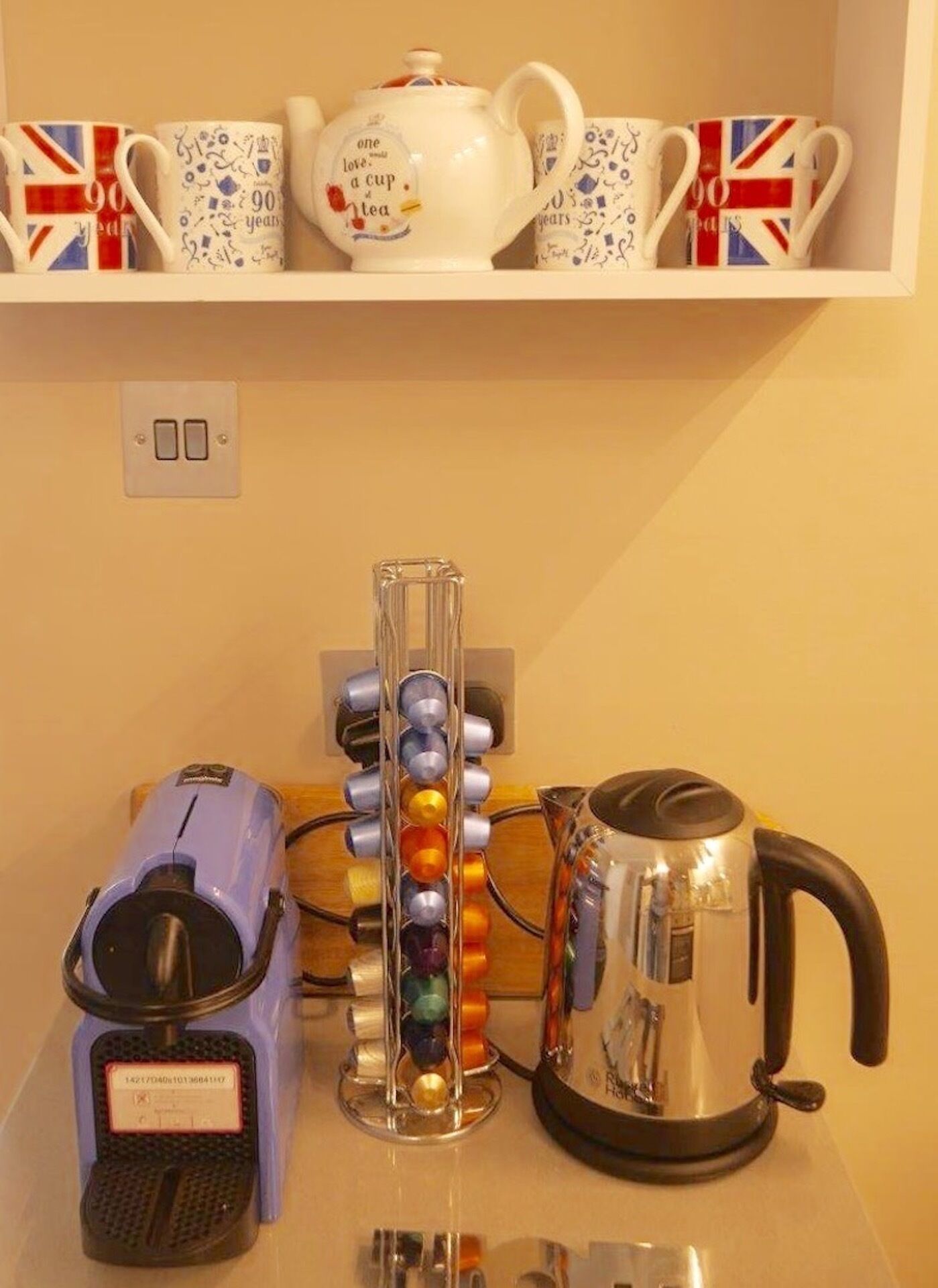 Une cuisine équipée d’une machine à café, d’une bouilloire et d’une étagère où sont rangées des tasses à thé et une théière.