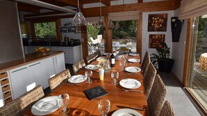 A dining area with a wooden table set for a meal, surrounded by wicker chairs, and a view of the outdoors through large windows. - Perfect location! Superb Chalet 5 *, jacuzzi and spectacular view  (Le Grand-Bornand)