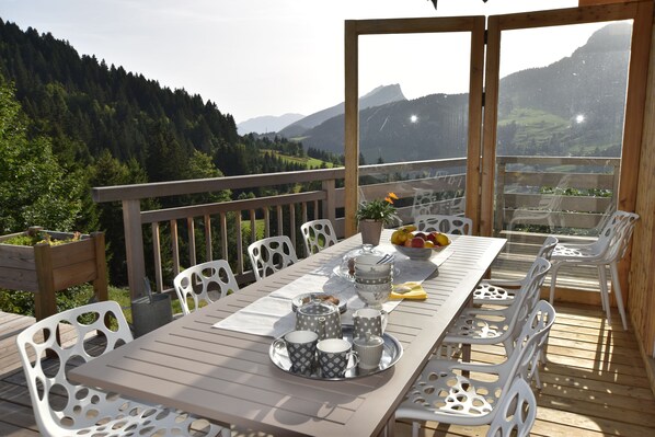 Eine Holzterrasse mit einem für das Frühstück gedeckten Tisch, mit Blick auf eine Berglandschaft.