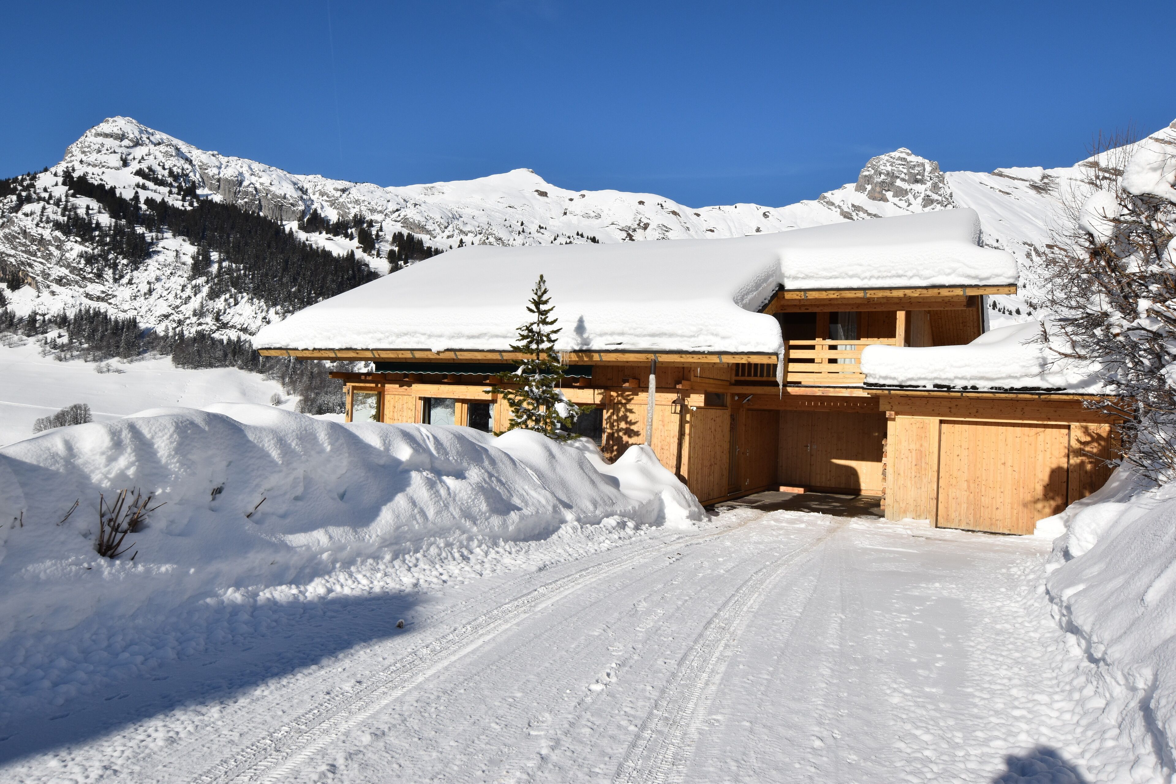 Un chalet en bois, dont le toit est recouvert de neige, entouré de montagnes enneigées et surplombant un ciel dégagé.