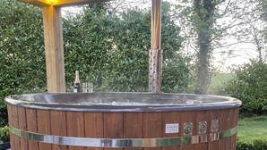 Ein hölzernes Whirlpool mit Metallgestell, umgeben von einer Holzterrasse und einem überdachten Bereich.