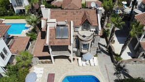 A large house with a swimming pool, multiple balconies, and a patio area with lounge chairs and umbrellas. - Calis Beach - Beautiful 4 bedroom villa with private pool and WiFi  (Fethiye)