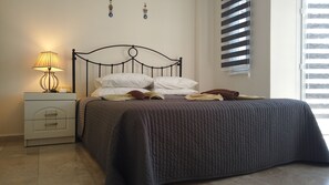 Een net opgemaakt bed met een donge deken, een bedlampje en een nachtkastje met een lamp.