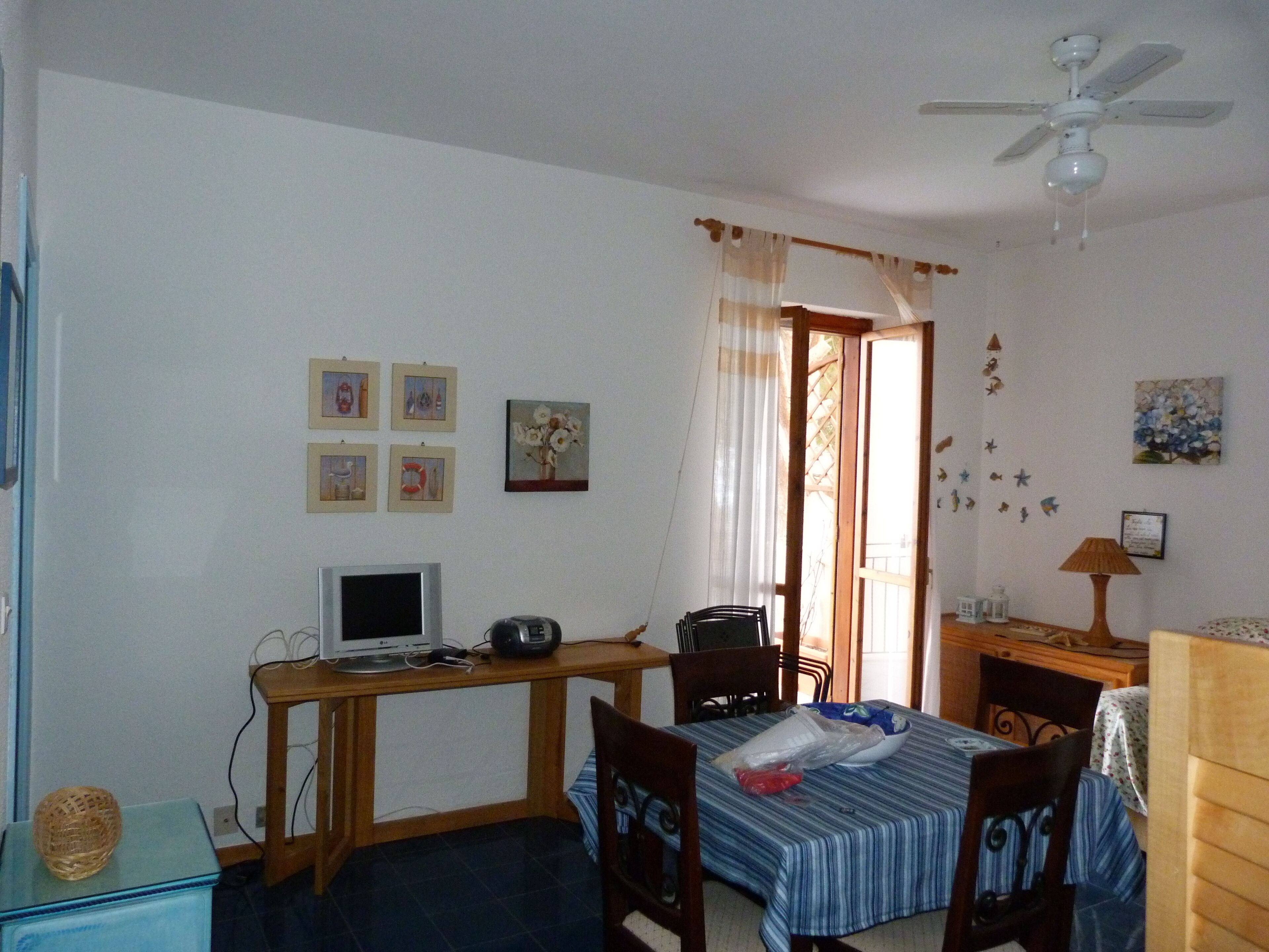 A room with a desk, computer, chair, bed, and a ceiling fan.