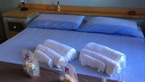 Een keurig opgemaakt bed met twee kussens en twee opgerolde handdoeken. Boven het bed hangen twee ingelijste zeesterren aan de muur.
