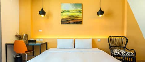 A hotel room with a large bed, two pendant lights, a desk with a chair, and a wall-mounted painting.