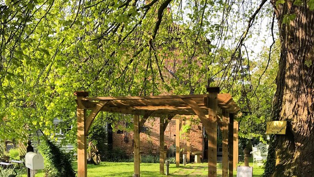 A wooden pergola in a garden with a gravel path, surrounded by greenery and a brick wall. - Riverside cottage in a beautiful garden in Lincolnshire. (Boston)