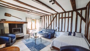 Una habitación tradicional con vigas de madera a la vista, chimenea, sofá, cama y mesa de centro.
