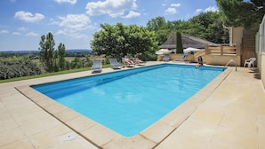 Una piscina rectangular con borde de azulejos, rodeada de sillas de descanso y un área de patio.