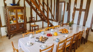 Un comedor con una mesa larga dispuesta para el desayuno, sillas de madera, un armario con puertas de cristal y una escalera.