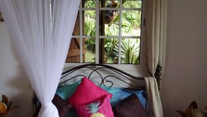 A bed with a canopy, pillows, and a window with a view of greenery. - The KREYOL LODGES presents its SUITE KAYOU ... view sea and mountain (DESHAIES)