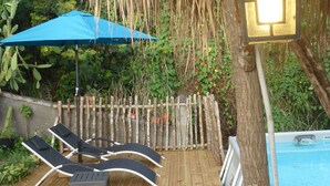 A wooden deck with lounge chairs and a blue umbrella, a pool, and a rustic wooden fence. - The KREYOL LODGES presents its SUITE KAYOU ... view sea and mountain (DESHAIES)