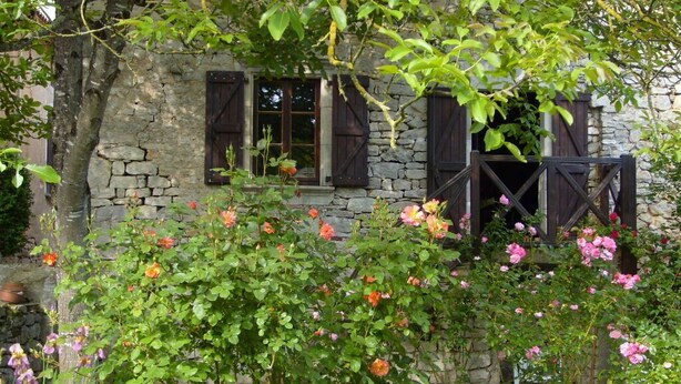 Un bâtiment en pierre au charme rustique, agrémenté d’un jardin où s’épanouissent des rosiers et où grimpent des lierres.