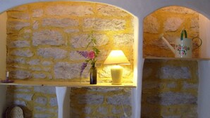 Un mur en pierre avec des étagères où sont rangés des livres et une lampe.