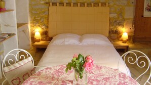 Une chambre avec un mur en pierre, une tête de lit en bois, deux lampes de chevet et une nappe à motifs floraux.