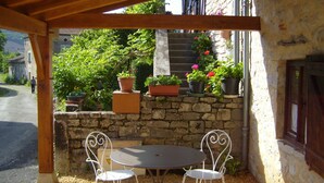 Un espace extérieur abrité, doté d’une terrasse, d’un mur en pierre, de plantes en pot et offrant une vue sur une rue et des bâtiments.