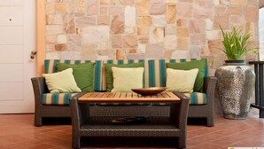 A room with a stone wall, wicker furniture, and a large vase. - GRANMONTE Wine Cottage (Pak Chong)